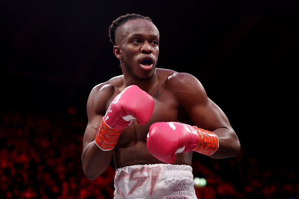 KSI, a Black man with short black hair, white sports shorts and red boxing gloves, strikes a boxing pose during a boxing fight.