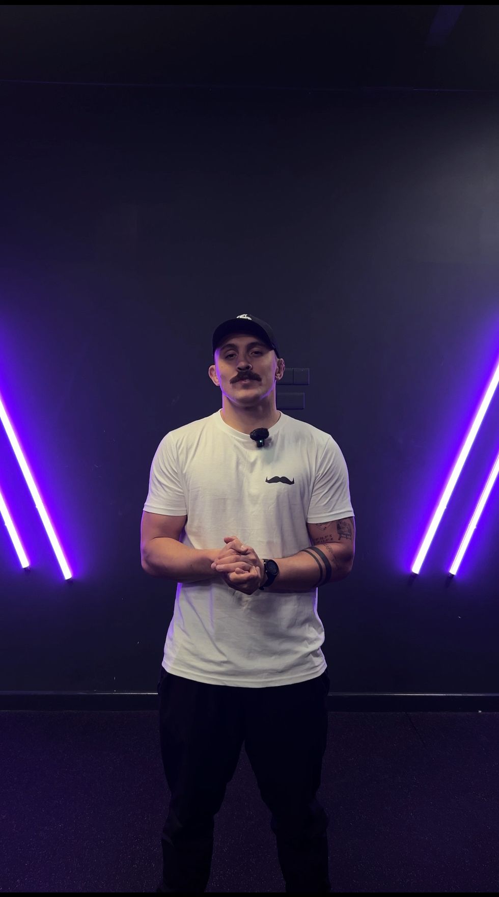 Man wearing white t-shirt and black cap stands in front of purple lights